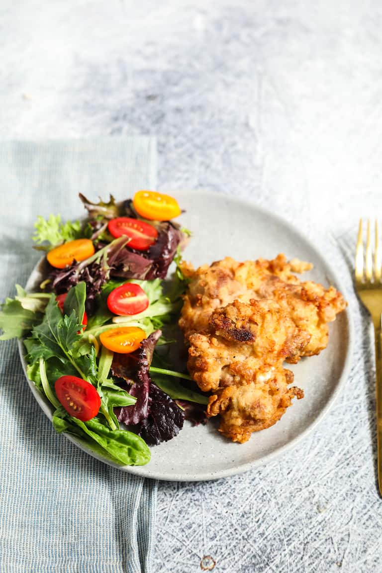 a plate of air fryer fried chicken and a green salad set next to a fork