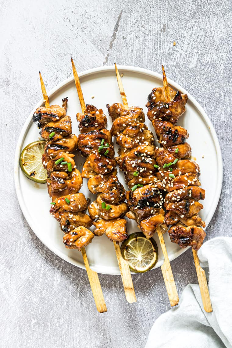 finished grilled chicken skewers on a white plate and garnished with grilled lime slices