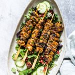 a platter filled with grilled chicken skewers served on top of a green salad