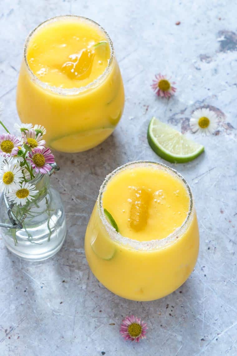 2 glasses mango margarita recipe on a table with flowers and lime