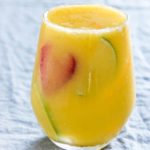 close up of a mango margarita inn a glass on a table