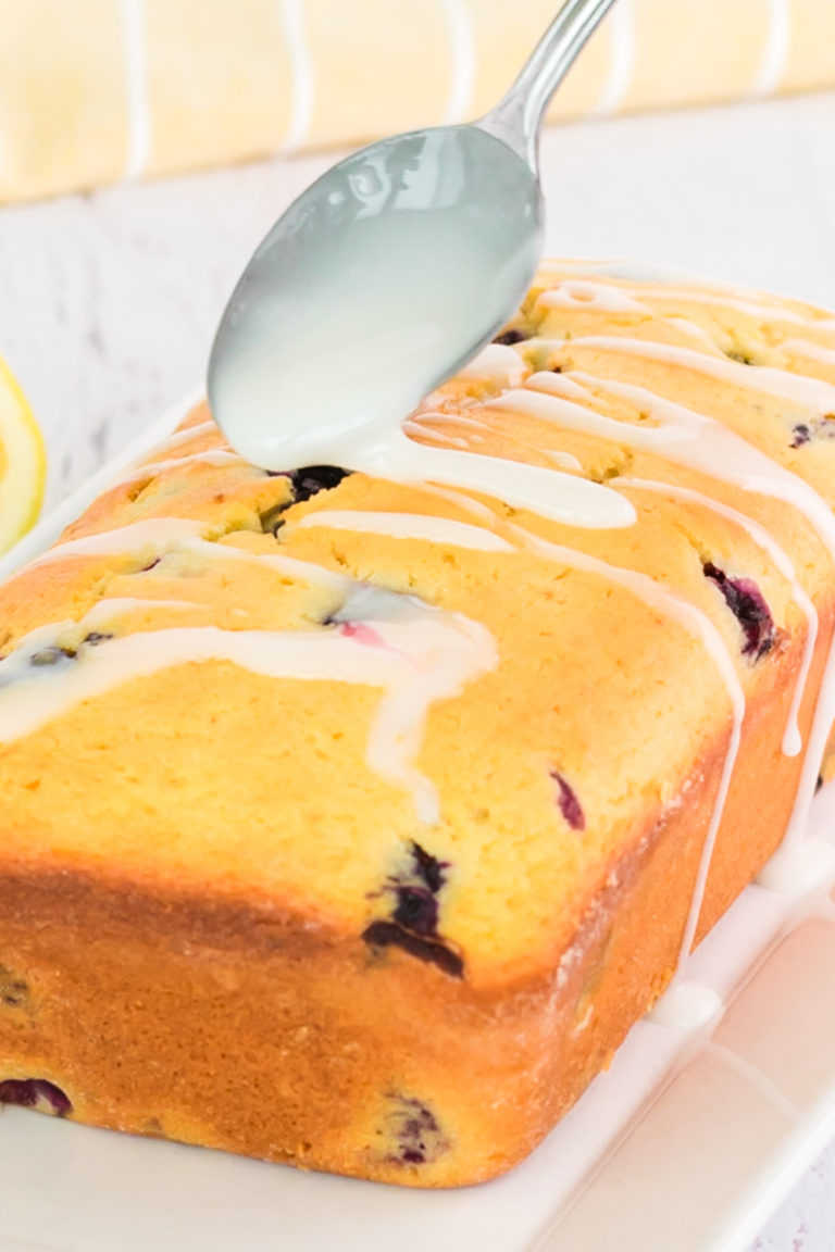 lemon glaze being drizzled on top of the completed blueberry lemon bread