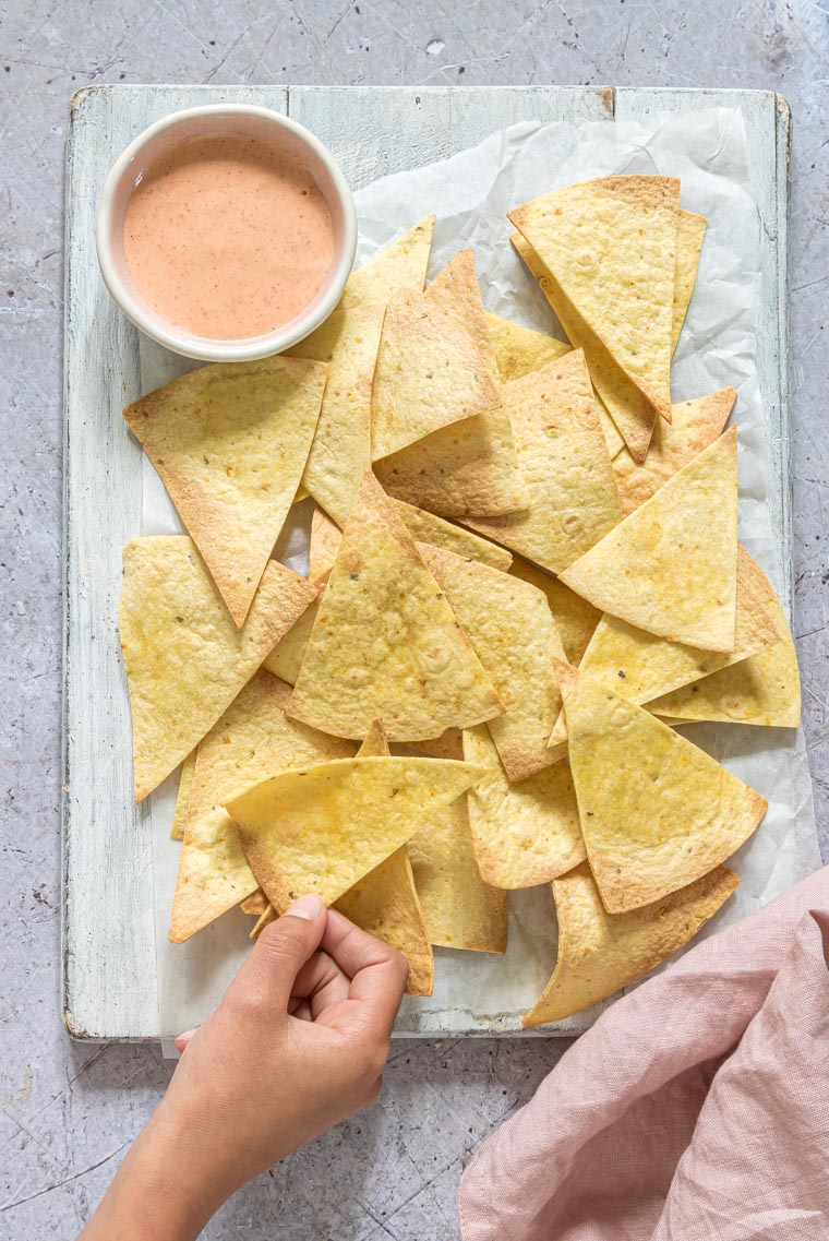 a hand taking some air fryer tortilla chips from a piece of parchment paper