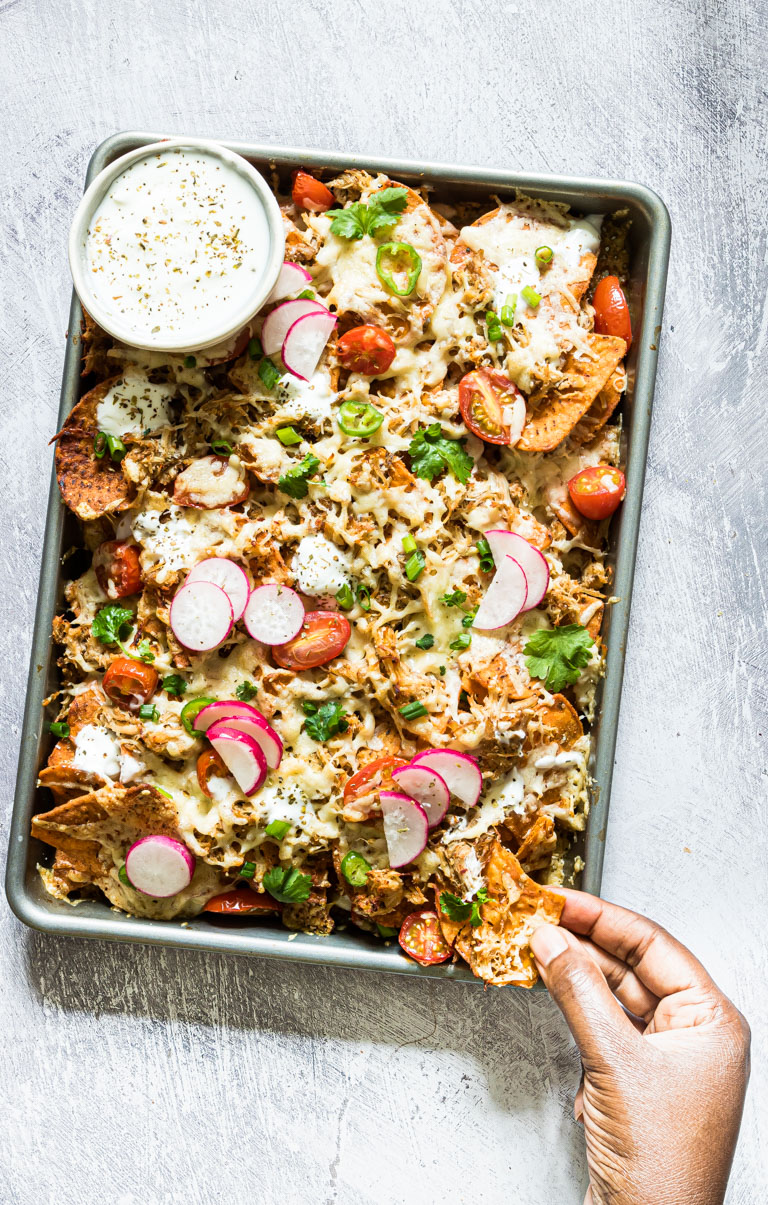 a hand removing some of the instant pot chicken nachos from a tray