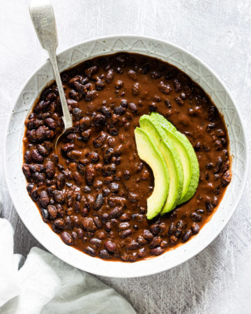 a bowl of instant pot black beans stew served with sliced avocado