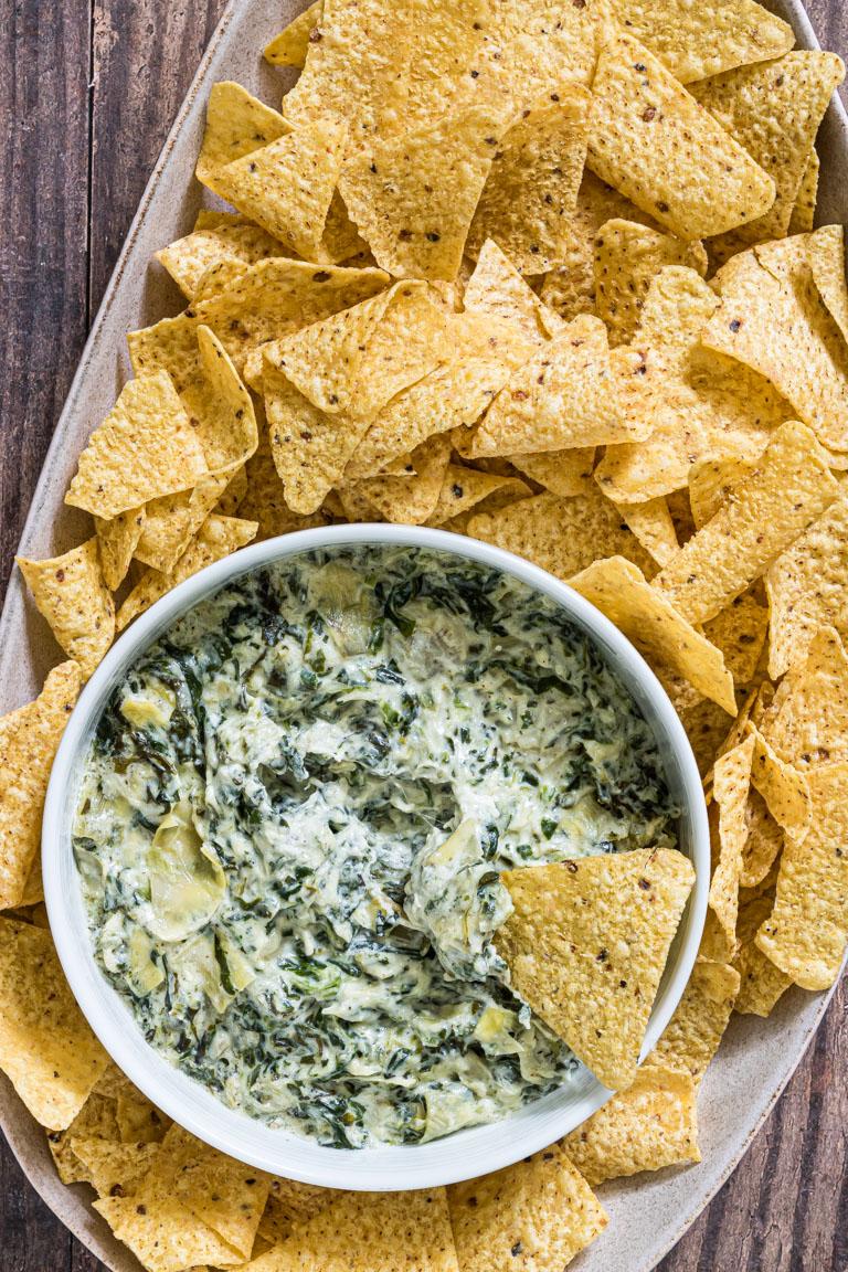 instant pot spinach artichoke dip in a white bowl with one tortilla chip dipped into it