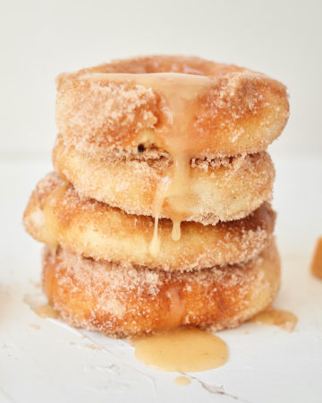 four air fryer caramel apple donuts stacked and drizzled with caramel sauce