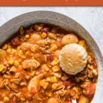 a round bowl of brunswick stew with a spoon and a biscuit in it