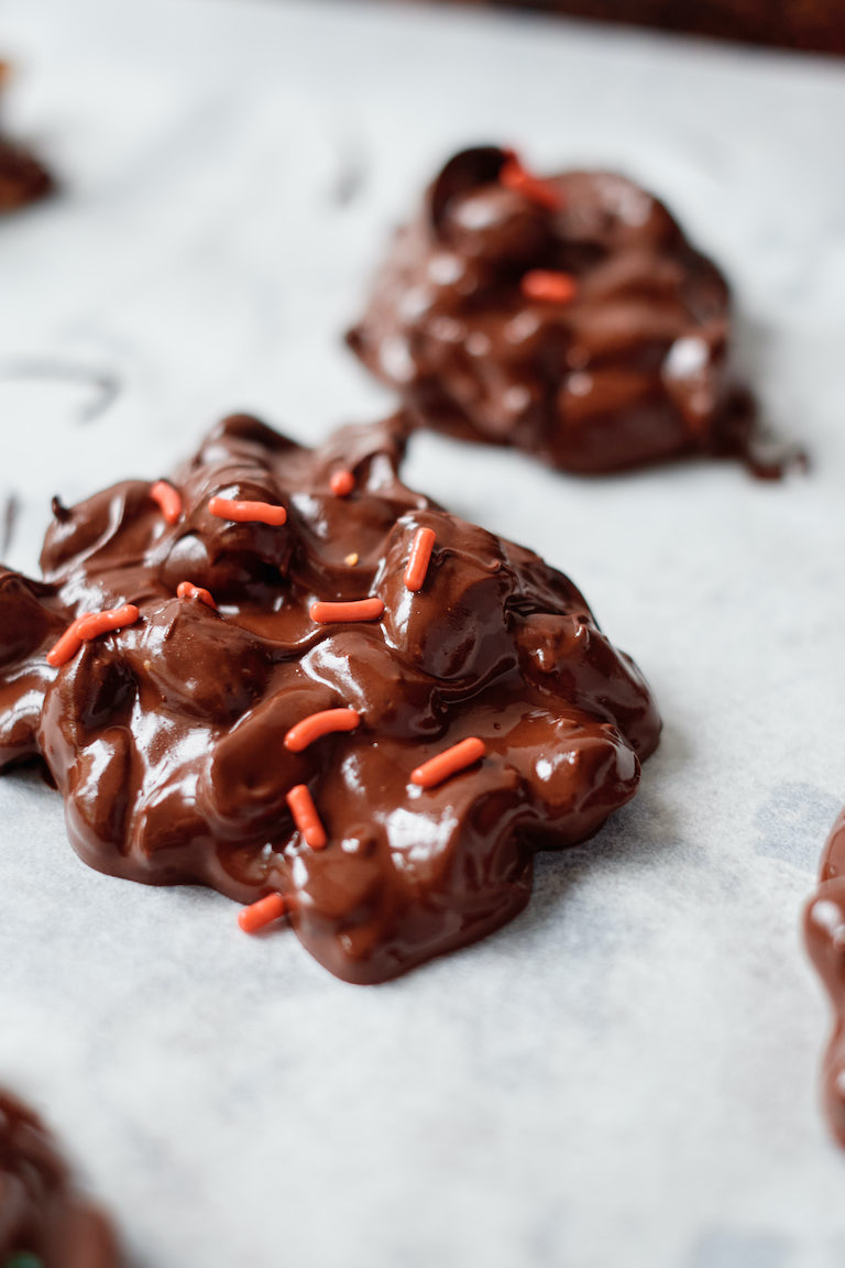 the crockpot Christmas candy clusters on a baking sheet with red sprinkles being applied