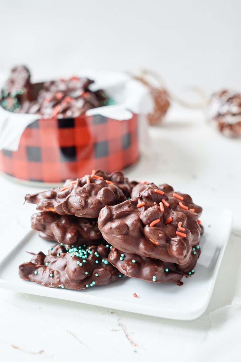 crockpot Christmas candy served on a white platter in front of a plaid holiday tin