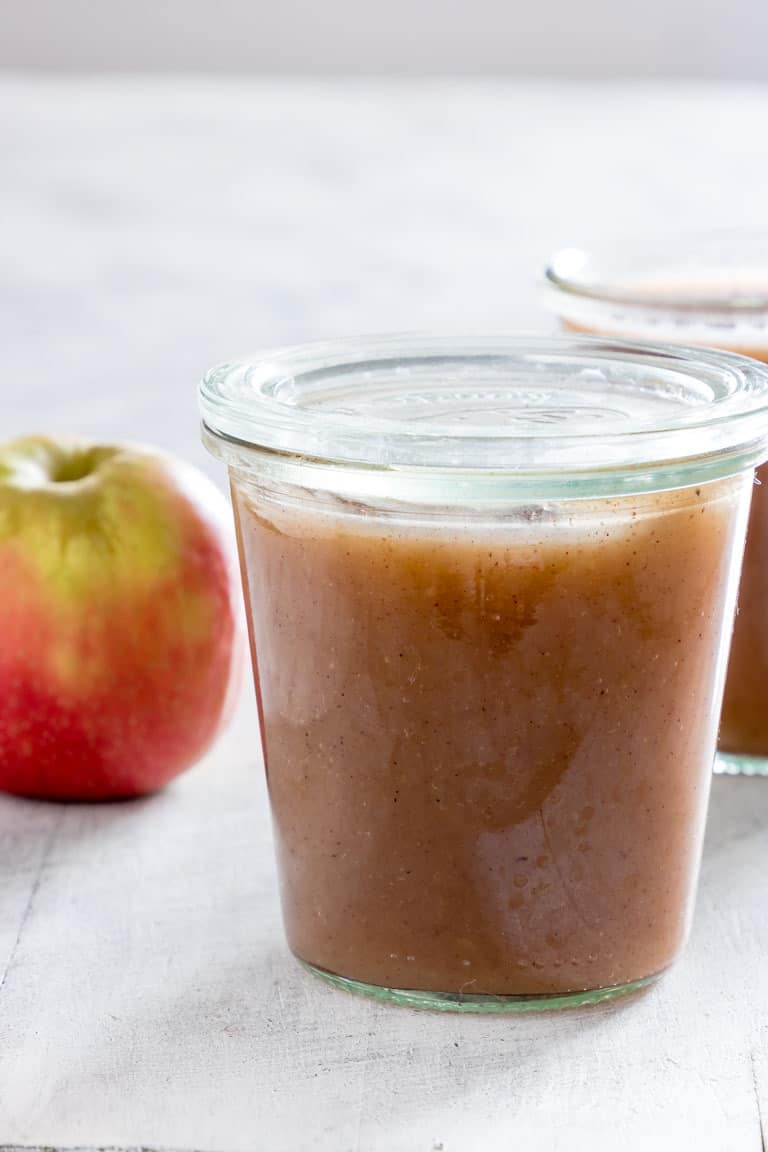 A jar full of Instant Pot Applesauce with apple and another jar in the background