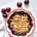 a dish of air fryer cherry crisp with spoon, napkin and fresh cherries