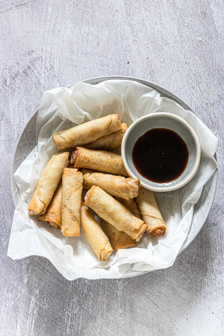 air fryer egg rolls next to a dish of soy dipping sauce