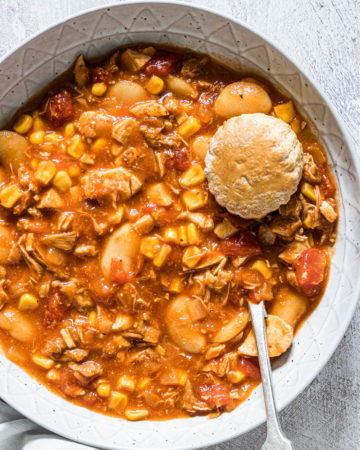 close up view of brunswick stew served in a blue bowl with a silver spoon