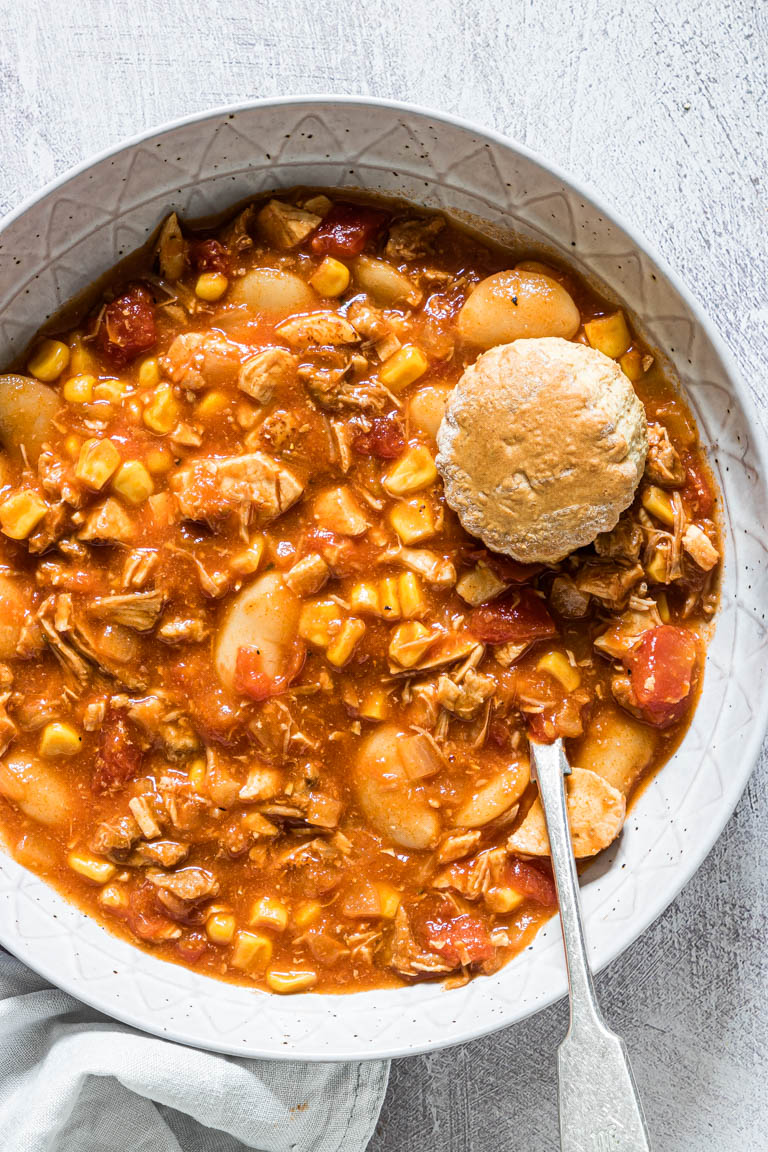 close up view of brunswick stew served in a blue bowl with a silver spoon