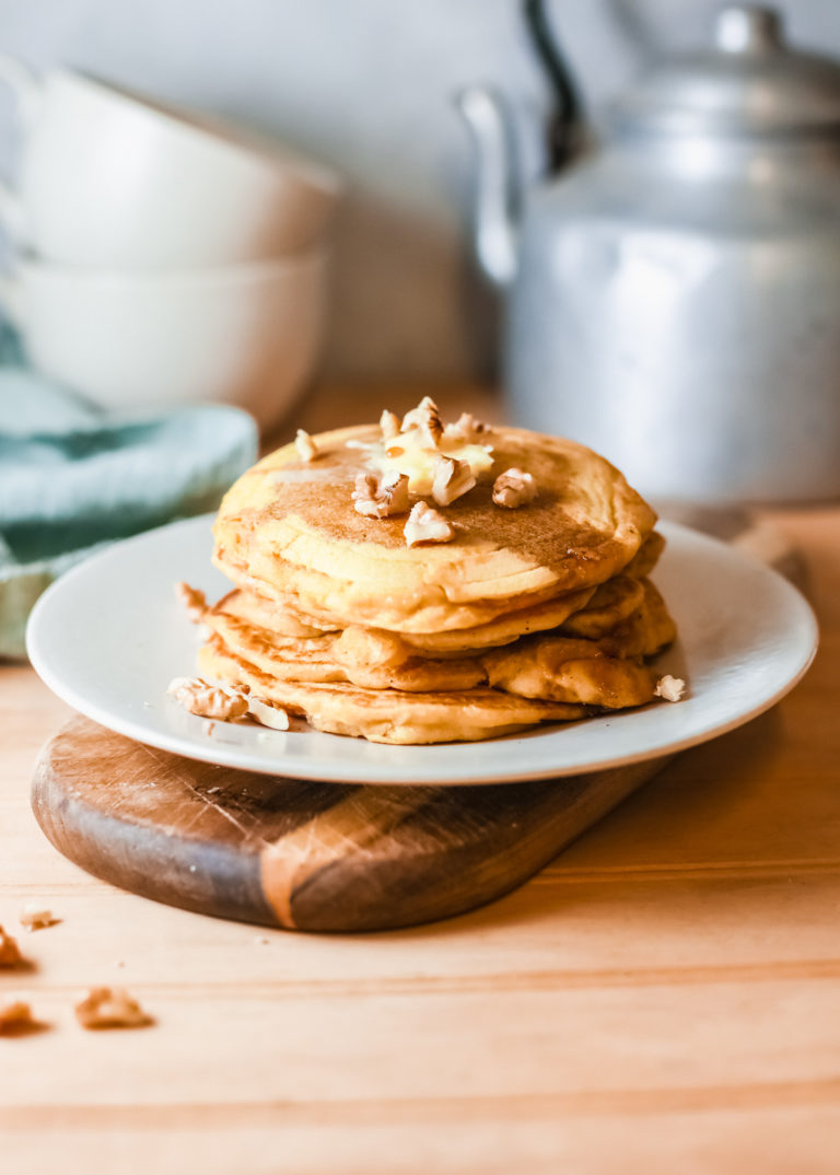 a stack of pumpkin pancakes on a white plate and topped with nuts and syrup