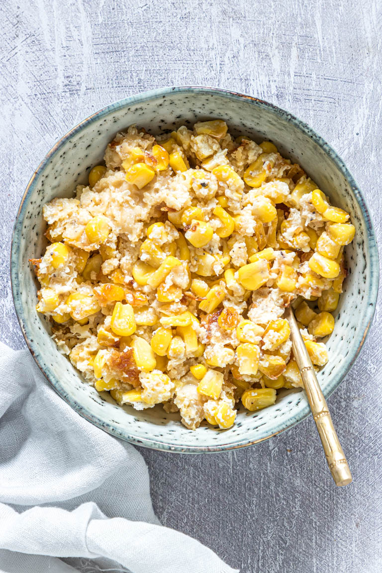 a serving of scalloped corn in a blue bowl with a gold spoon