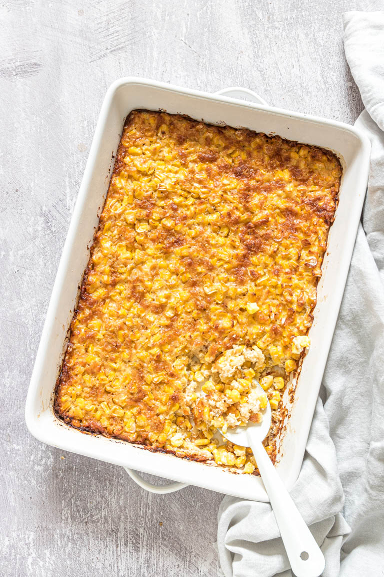 the cooked scalloped corn casserole inside a baking dish with a spoon removing a portion