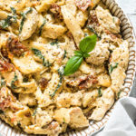a bowl of slow cooker pasta tuscan chicken garnished with fresh basil and served with a cloth napkin