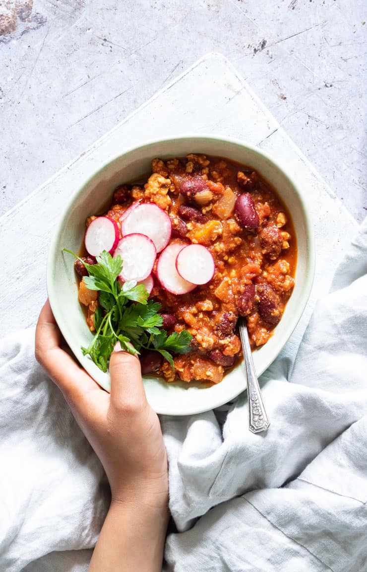 a hand holding a white bowl filled with slow cooker turkey chili