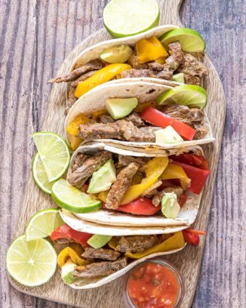 a wooden cutting board filled with completed instant pot steak fajitas
