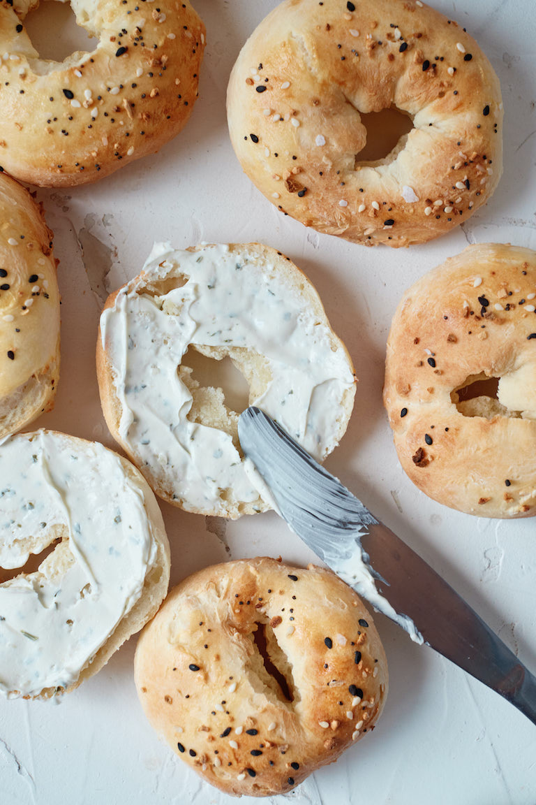 top down view of cooked bagels with one sliced open and a knife spreading cream cheese onto it