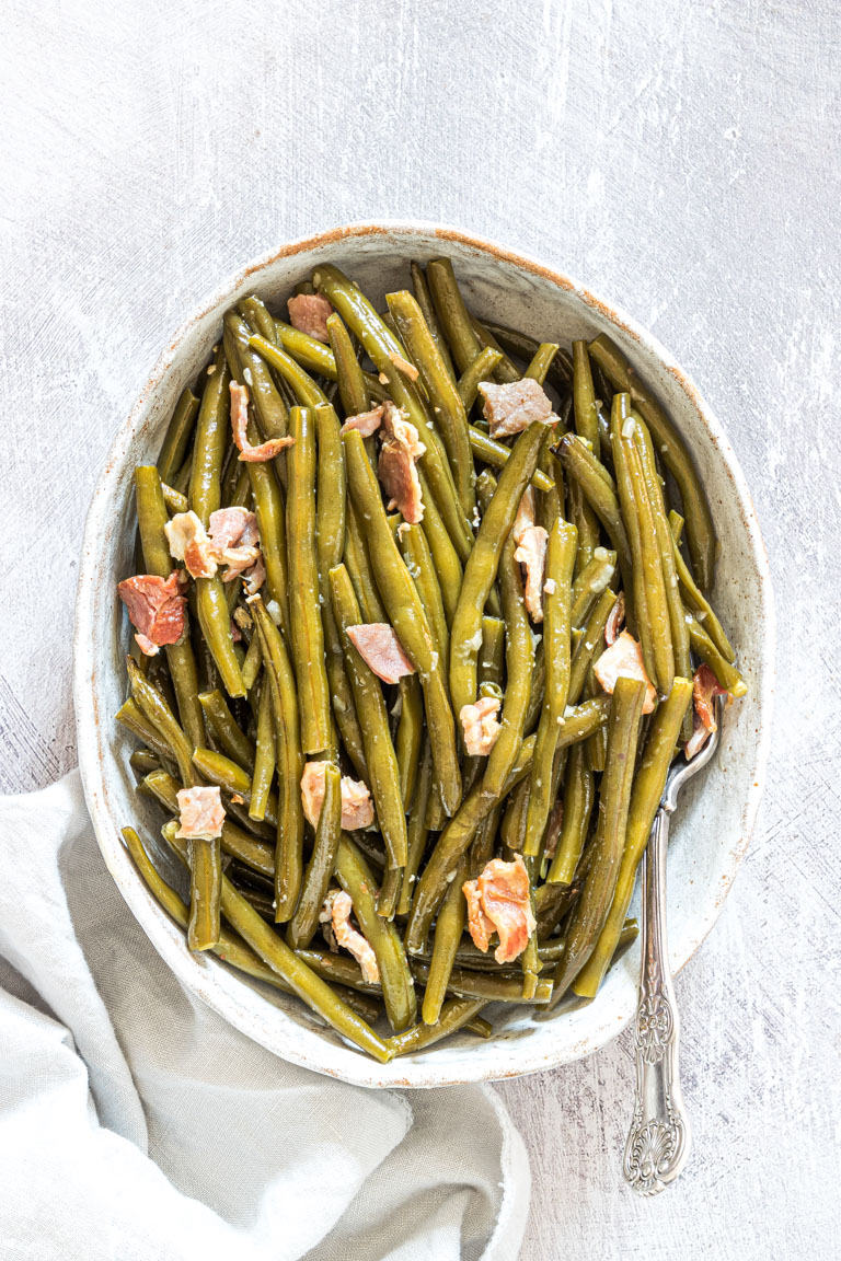 the finished crockpot green beans served in a white dish with a silver spoon