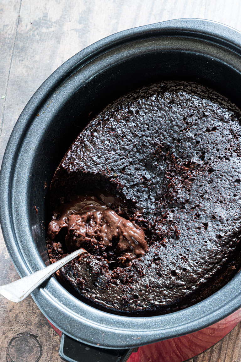 the finished lava cake recipe inside the crockpot with a serving spoon stuck in it