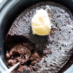 the finished crockpot lava cake inside the slow cooker with a scoop of ice cream on top and a serving spoon stuck inside.
