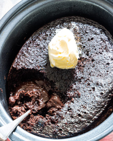 the finished crockpot lava cake inside the slow cooker with a scoop of ice cream on top and a serving spoon stuck inside