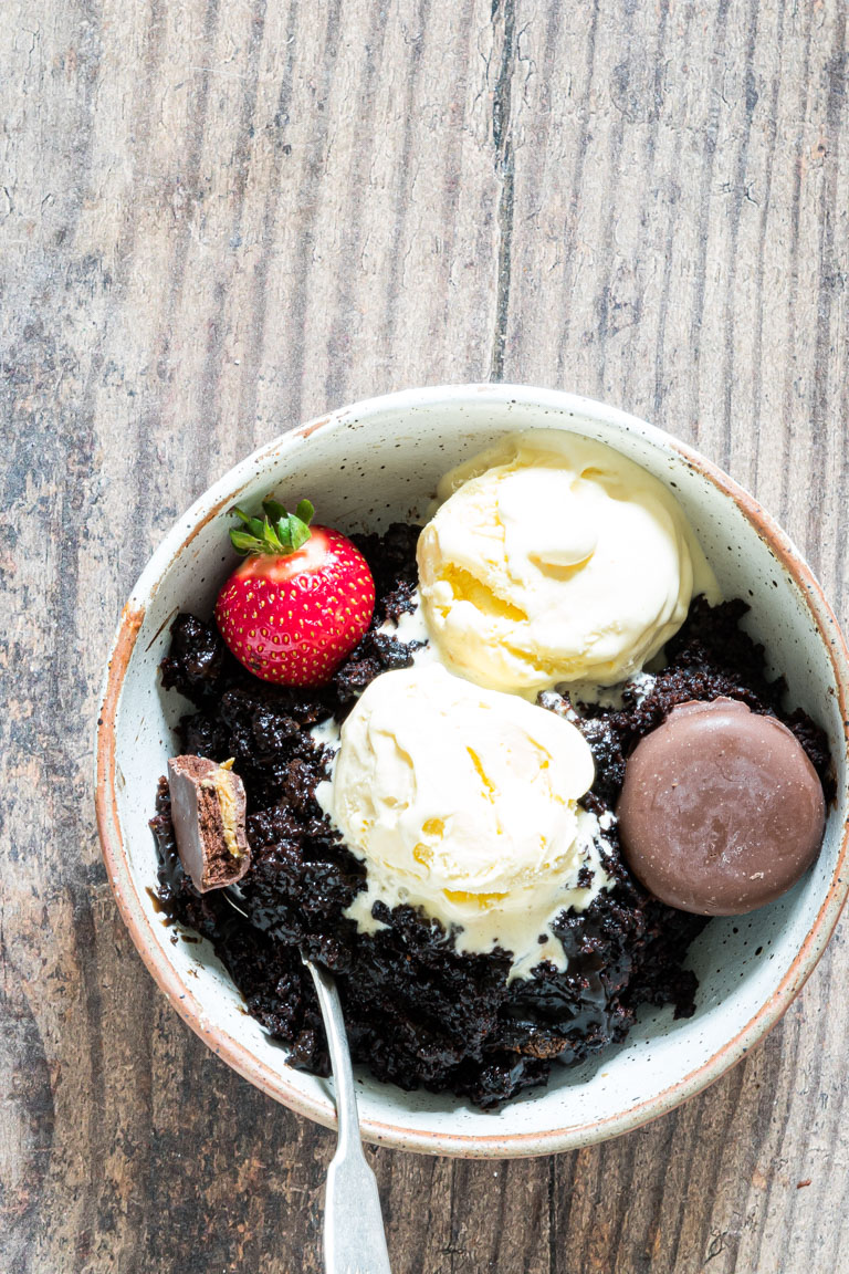 one portion of chocolate lava cake in a bowl and topped with ice cream, whipped cream and berries