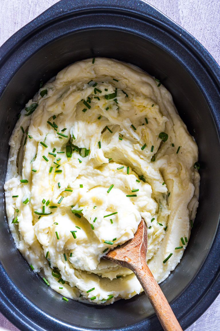 slow cooker mashed potatoes inside the slow cooker with a wooden spoon stuck inside.