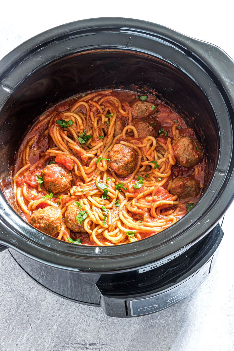 close up of slow cooker spaghetti and meatballs in the slow cooker with garnishes