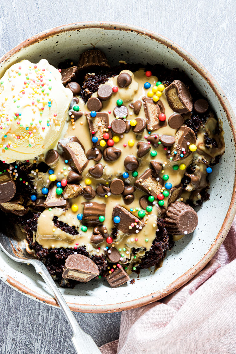 a serving of crock pot chocolate peanut butter cake topped with a scoop of ice cream and candy sprinkles