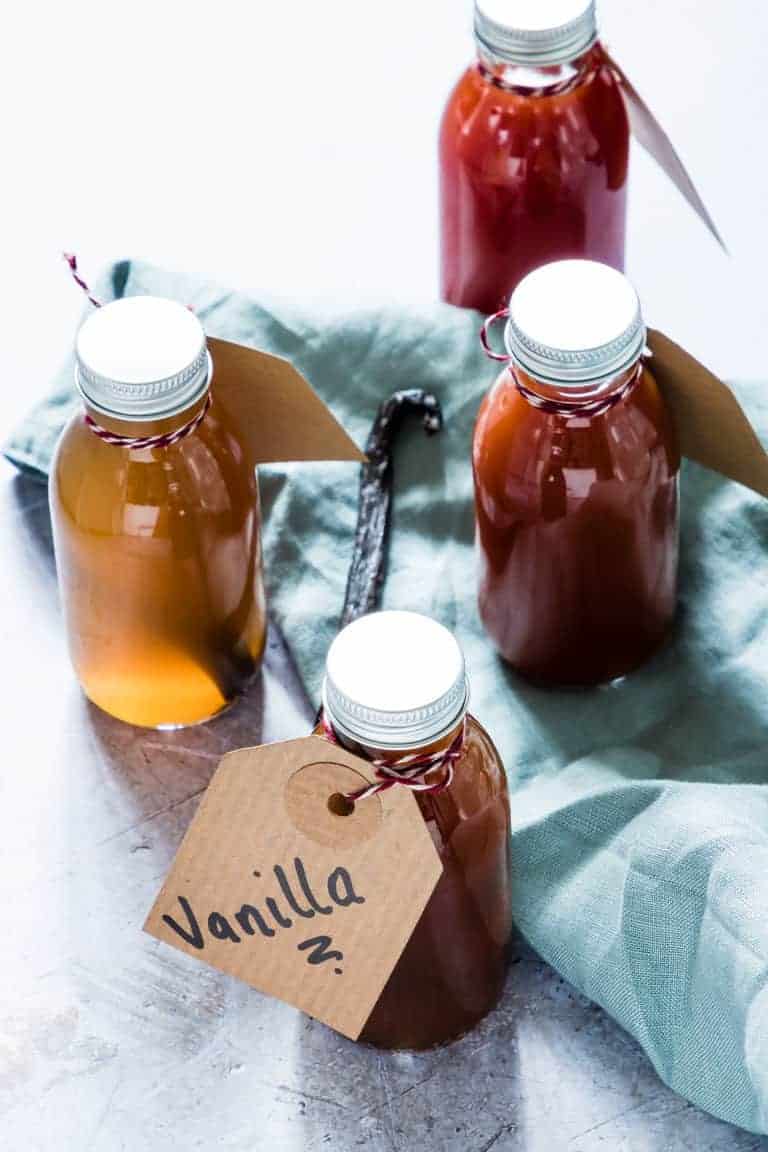 The completed Instant Pot Vanilla Extract poured into individual bottles and tied with a handwritten gift tag sitting on a blue cloth dish towel