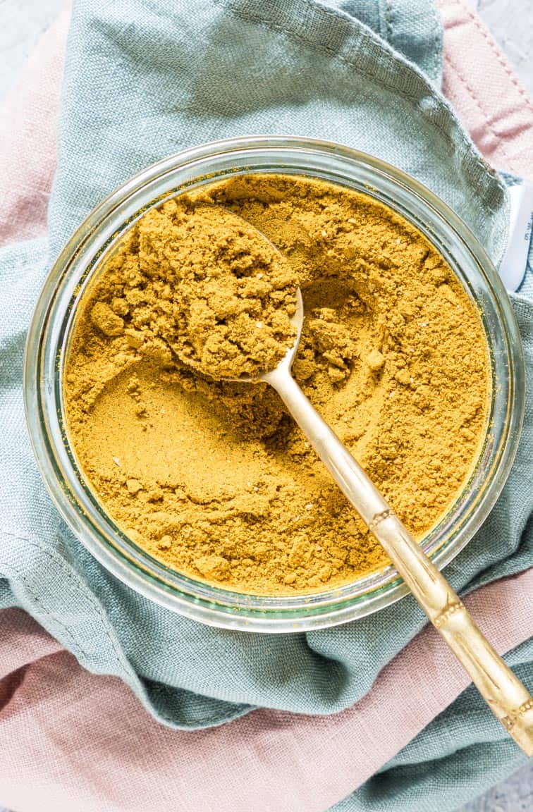 close up view of jar filled with Jamaican Curry Powder with a gold spoon