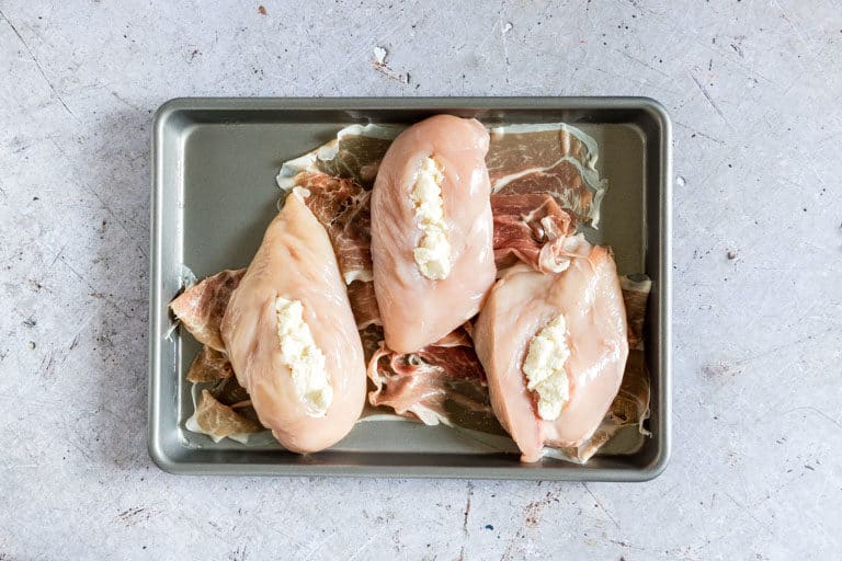 three chicken breasts set on top of slices of Proscuitto de Parma placed on a baking sheet for making proscuitto wrapped chicken