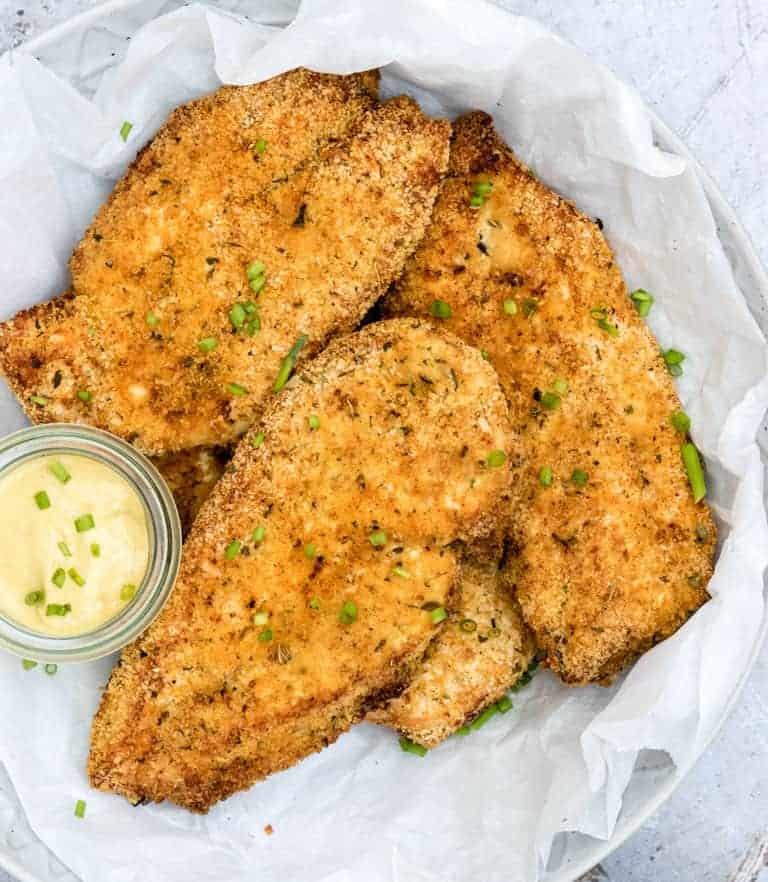 Close up of the cooked Air Fryer Boneless Chicken Breasts on parchment paper and ready to serve with a side of dipping sauce