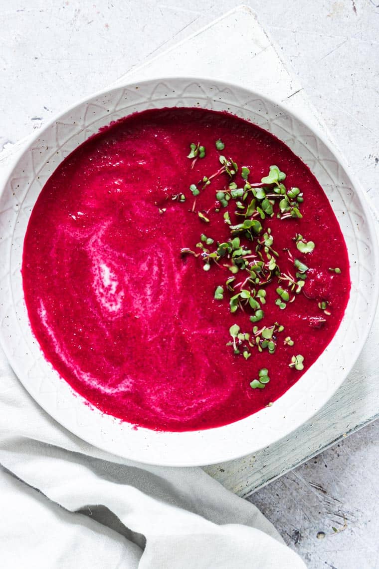 Thai curry beetroot soup garnished with herbs and served in a white bowl