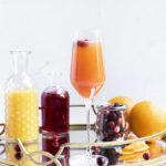 a finished cranberry mimosa on a serving try along with all of the ingredients