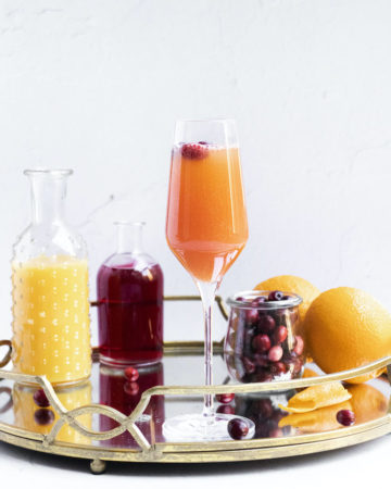 a finished cranberry mimosa on a serving try along with all of the ingredients