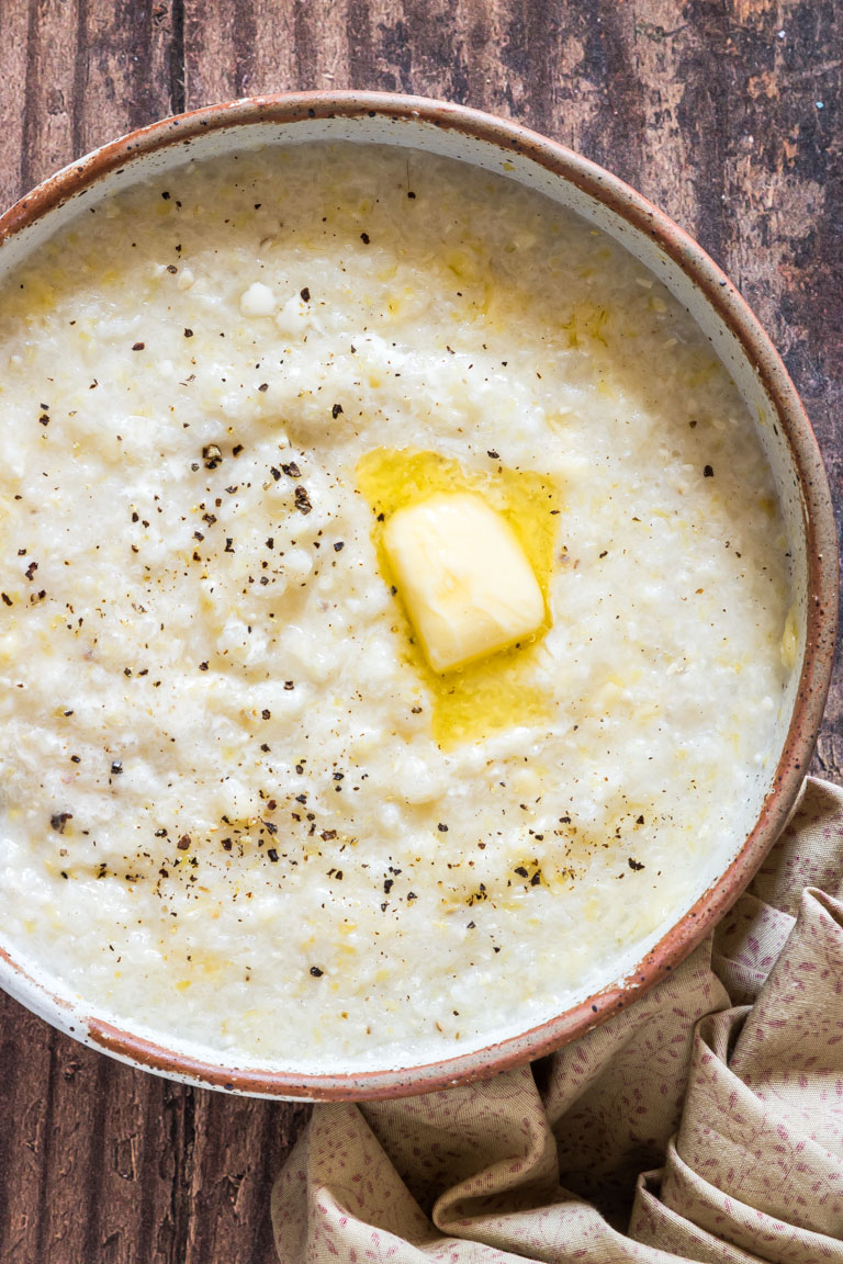 close up view of the completed slow cooker grits served in a bowl and topped with butter