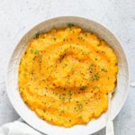 crockpot mashed butternut squash served in a white bowl and topped with herbs