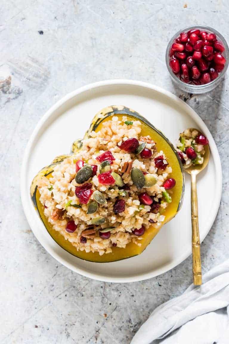 One serving of Instant Pot Stuffed Squash on a white plate served with a gold spoon and next to a small glass dish of pomegranate seeds