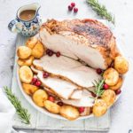 finished air fryer turkey breast on a serving platter with potatoes and cranberries and a pitcher of gravy