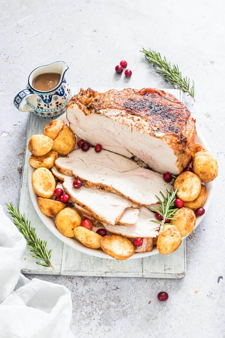 finished air fryer turkey breast on a serving platter with potatoes and cranberries and a pitcher of gravy