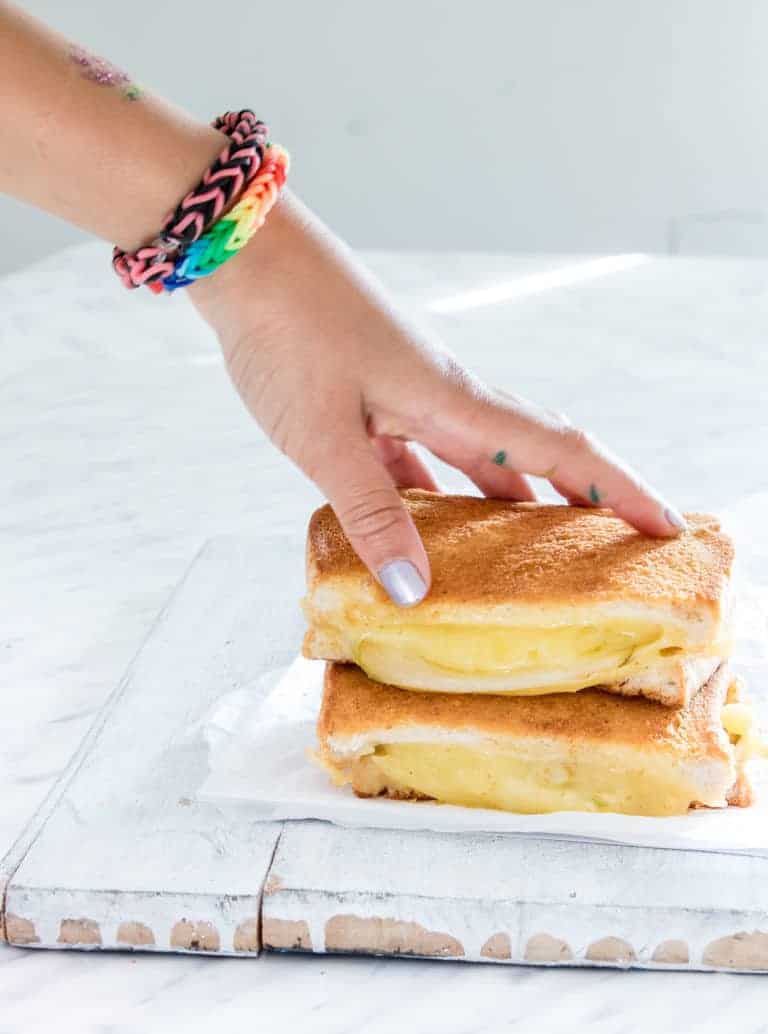 two halves of Grilled Cheese in  Air Fryer stacked on top of each other with a kid's hand picking up the top half.