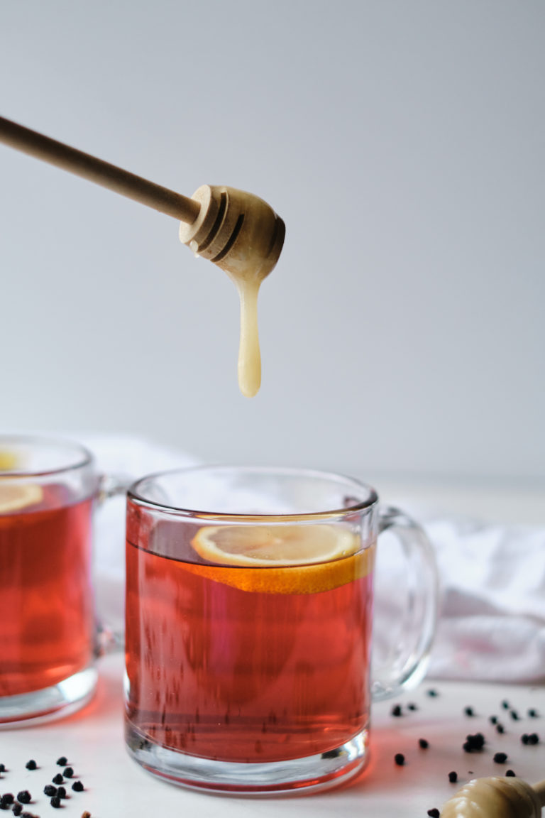 a mug of elderberry tea with honey being drizzled into it.