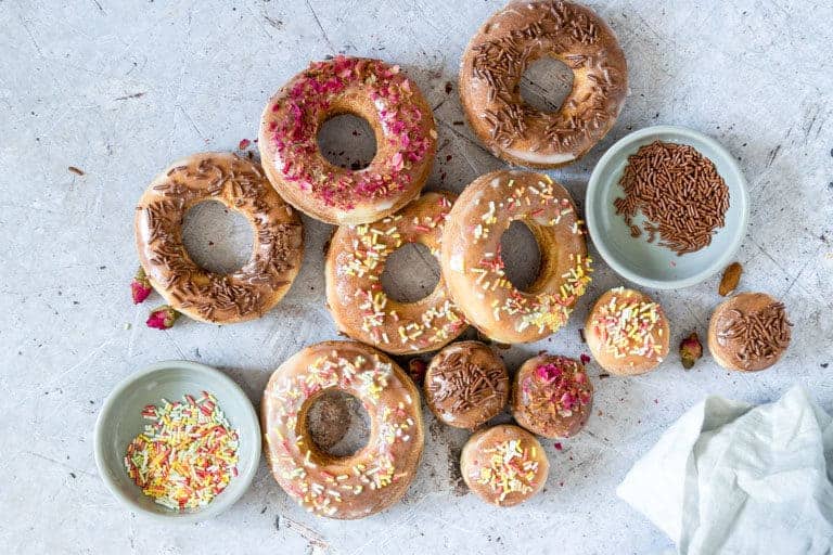 Air Fryer Donuts with various toppings set next to small bowls filled with sprinkles and dried edible flowers