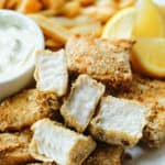 close up view of a serving of fish sticks on a white plate with lemon wedges and tartar sauce